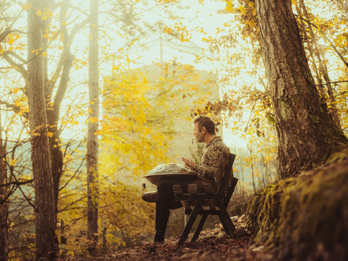 Musicien jouant du handpan sur un banc, en forêt