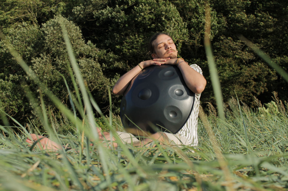 Homme appuyé sur un handpan dans les herbes hautes